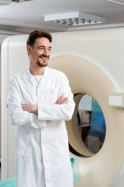 radiologo sorridente in piedi vicino tomografia computerizzata scanner e guardando altrove - Foto, immagini