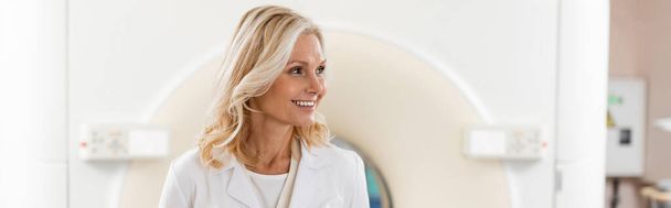 szczęśliwy blond radiolog patrząc daleko w pobliżu maszyny tomografii komputerowej, baner - Zdjęcie, obraz