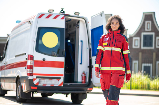 Young African American emergency doctor in the red uniform moving away from the ambulance van - Valokuva, kuva