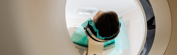 взрослый брюнетка мужчина делает диагностику на компьютерной томографии сканер в клинике, баннер - Фото, изображение