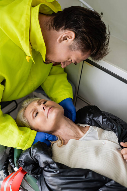 High angle view of paramedic checking neck of middle aged patient in emergency vehicle  - Foto, imagen