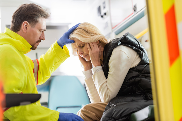 Paramedic in latex gloves touching head of middle aged woman in emergency car  - Φωτογραφία, εικόνα