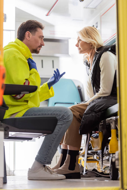 Vue latérale de gestes paramédicaux et de parler à une femme d'âge moyen inquiète dans un véhicule d'urgence  - Photo, image