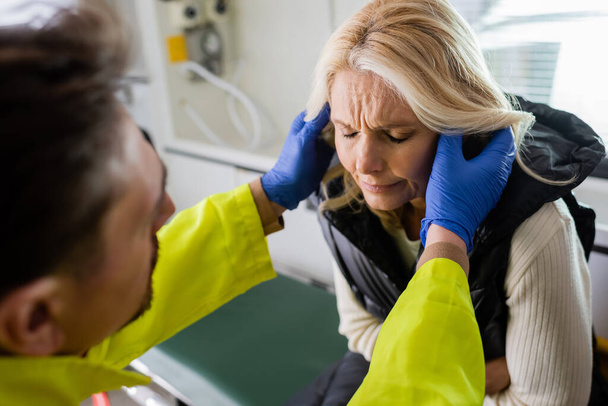 ambulancier flou dans des gants en latex vérifier la tête de la femme d'âge moyen dans la voiture d'urgence  - Photo, image