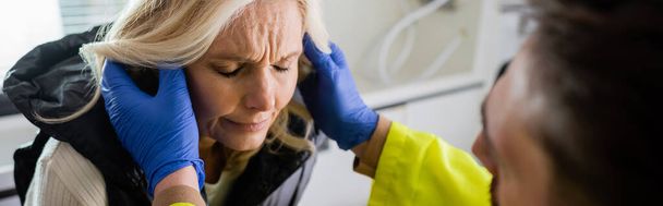 Ensihoitaja tarkistaa tyytymättömän keski-ikäisen naisen pään hätäajoneuvossa, banneri  - Valokuva, kuva