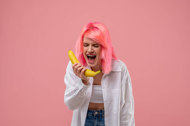 Young female with a tongue piercing and braces performing a song with the fruit microphone - Photo, Image