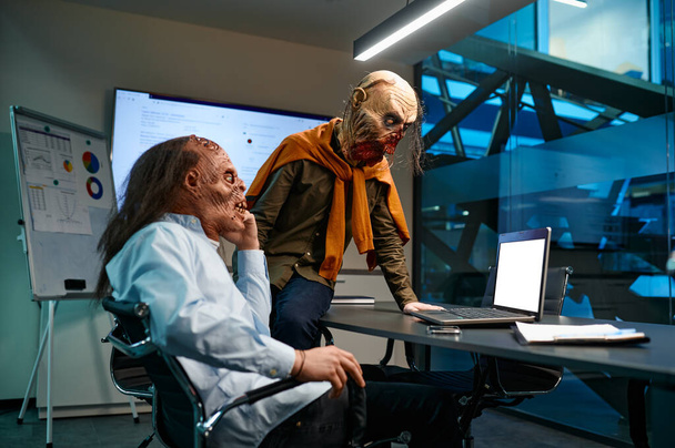 Dwóch biznesmenów zombie na wideo czacie. Brzydki potwór korporacyjny za pomocą komputera do konferencji internetowej patrząc na ekranie laptopa. Biuro nocne sala konferencyjna wnętrze - Zdjęcie, obraz