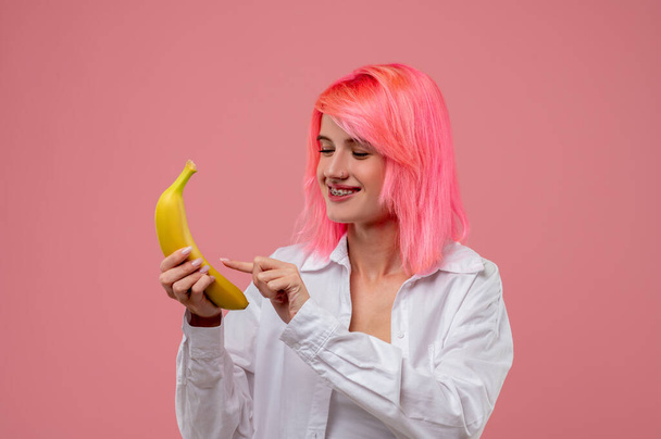 Smiling cute young woman with the metal braces and a nose ring tapping on the banana smartphone - Fotoğraf, Görsel