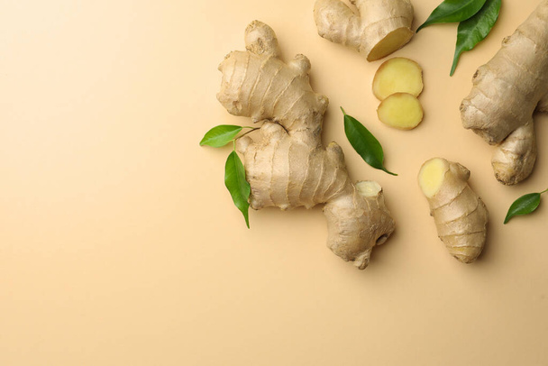 Fresh ginger with green leaves on beige background, flat lay. Space for text - Foto, imagen