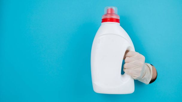 A woman is holding a white bottle of detergent. Womans hand sticking out of blue paper background - Foto, Imagen