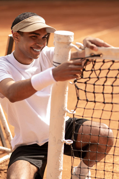 At the tennis courts. Smiling young sportsman fixing the net at the tennis courts - Foto, Imagen