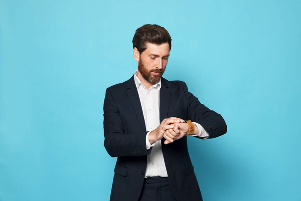 Handsome bearded man looking at wristwatch on light blue background - Fotoğraf, Görsel
