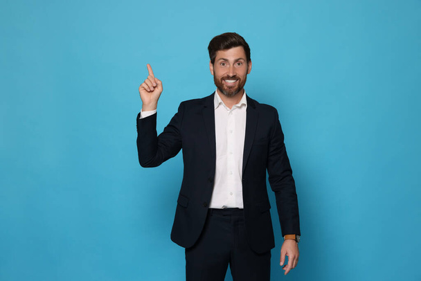 Smiling bearded man pointing index finger up on light blue background - Photo, image