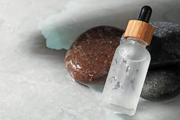Bottle of face serum and spa stones on wet grey marble table, closeup. Space for text - Fotografie, Obrázek