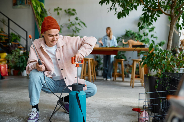 Man florist preparing sprayer for plants leaves misting. Couple working at floral workshop. Family startup business concept - 写真・画像