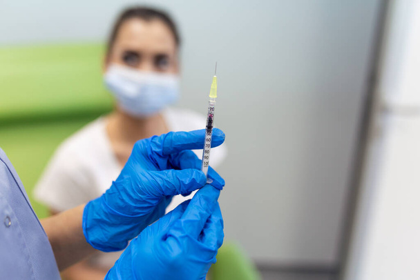 Lekarz trzymający strzykawkę wytwarzającą covid 19 dawek szczepionki w ramię pacjentki noszącej maskę. Koncepcja badań klinicznych przeciwko grypie, leczenie wirusem korony, widok z bliska. - Zdjęcie, obraz