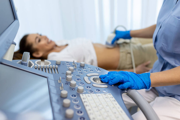 Widok boczny portrety ginekologa w białym fartuchu laboratoryjnym i sterylnych rękawic za pomocą skanera ultrasonograficznego podczas badania pacjentki. kobieta leżąca na leżaku na rozmytym tle - Zdjęcie, obraz