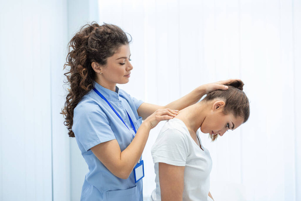 Licensed chiropractor or manual therapist doing neck stretch massage to relaxed female patient in clinic office. Young woman with whiplash or rheumatological problem getting professional doctor's help - Photo, Image