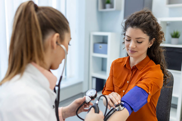血圧の測定。若い女性は現代の診療所で女性医師と面会している。血圧の測定。圧力計。高血圧と高心拍数 - 写真・画像