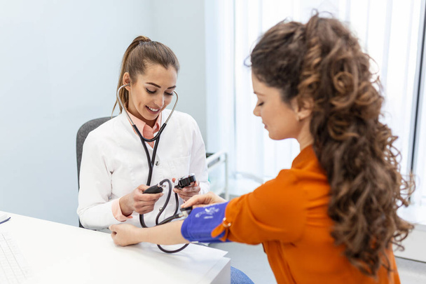 Verpleegster meten van de bloeddruk van een vrouw patiënt tijdens een onderzoek in de kliniek. Dokter controleert de bloeddruk van de patiënt. Gezondheidszorg. - Foto, afbeelding
