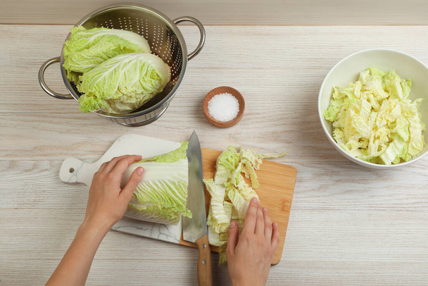 Woman cutting Chinese cabbage at white wooden kitchen table, top view - Fotoğraf, Görsel