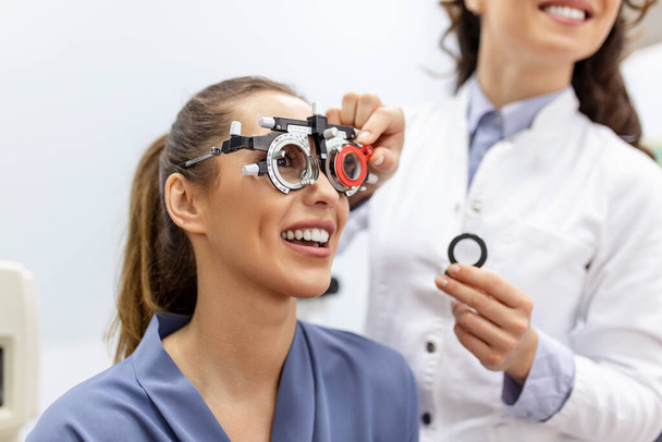 Οφθαλμολογικά που εξετάζει γυναίκα με οπτικό πλαίσιο οπτομέτρης. γυναίκα ασθενής να ελέγξει την όραση στην οφθαλμολογική κλινική. - Φωτογραφία, εικόνα