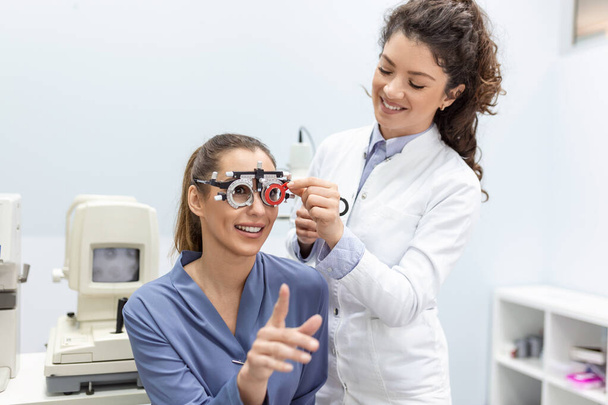 Οι οπτομετρητές αλλάζουν τους φακούς στο πλαίσιο της δοκιμής για να εξετάσουν την όραση της νεαρής γυναίκας στην οφθαλμολογική κλινική, επιλεκτική εστίαση - Φωτογραφία, εικόνα