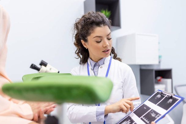婦人科医は、オフィスでの医療相談中の女性の健康の特徴を説明し、若い女性患者に超音波で画像を示しています - 写真・画像
