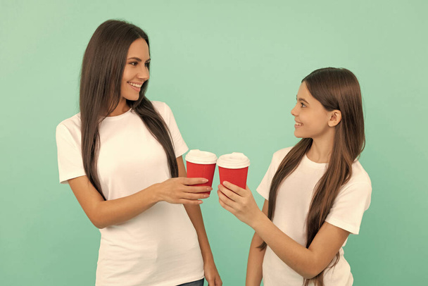 happy mother and daughter hold takeaway coffee on blue background. cheers. - 写真・画像