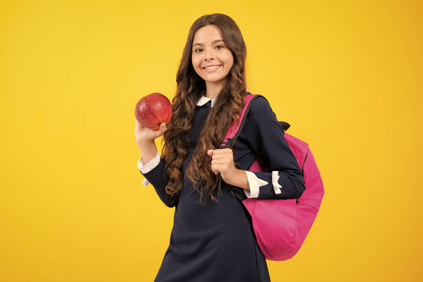 Возвращайся в школу. Подростковая школьница с рюкзаком держит яблоко готовым к обучению. Школьные дети с сумкой на изолированном желтом фоне студии - Фото, изображение