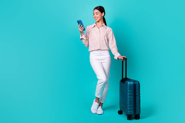 フルサイズ写真のかなり正日本人女性ホールド使用電話スーツケース隔離された電話色背景. - 写真・画像