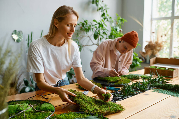 Professional florists working at creative art studio. Focus on young woman making composition from green fresh moss - Foto, Imagem