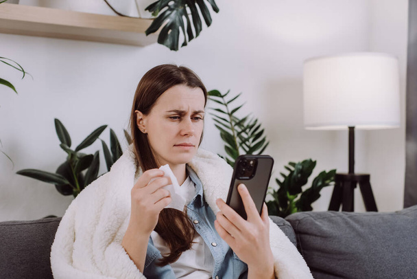 Sick young brunette lady patient sitting on couch at home talk to doctor on cellphone videocall conference medical app in telehealth telemedicine online service hospital quarantine social distance - Foto, imagen