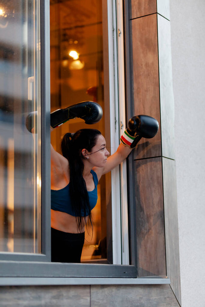 フィット女の子でボクシング手袋リラックスし、運動から休憩中に窓の外を見る. - 写真・画像