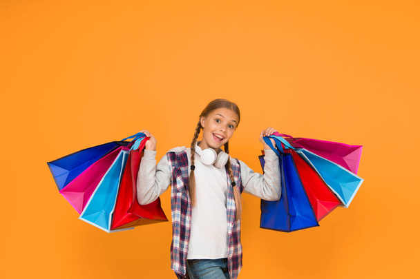 Holiday preparation and celebration. Shopping and sale on black friday. Addicted consumer. Dive into shopping. Happy child with paper bags. Little girl smile with shopping bags on yellow background. - Fotografie, Obrázek