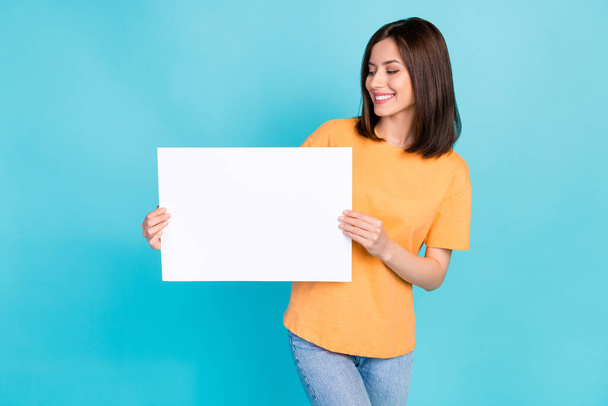 Foto van vrij positieve dame dragen oranje kleding houden papier blad kijken lege ruimte geïsoleerd op blauwe kleur achtergrond. - Foto, afbeelding
