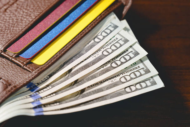 Száz dolláros bankjegyek egy bőrbarna pénztárcában az asztalon. Magas látószögű. - Fotó, kép