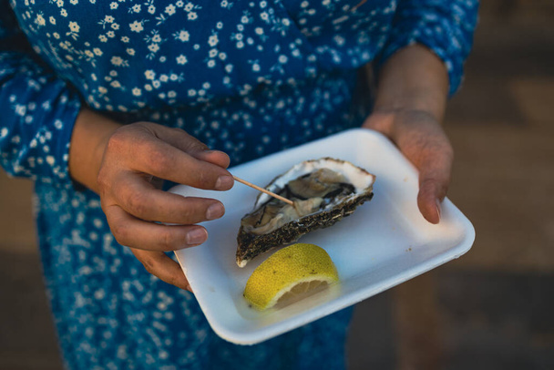 Close-up vrouwelijke hand houden take away food tray met verse geopende oester en citroen plakjes op straat voedsel markt, festival, evenement. Selectieve focus. Valencia, Spanje, Europa. - Foto, afbeelding