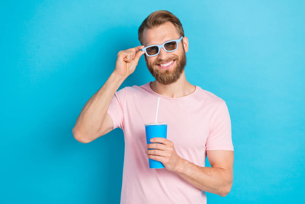Photo of good mood cute man wear pink t-shirt dark glasses drinking cold soda isolated blue color background. - Photo, Image