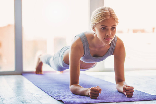 Belle jeune femme en tenue de sport faisant des exercices de planche sur tapis de yoga - Photo, image