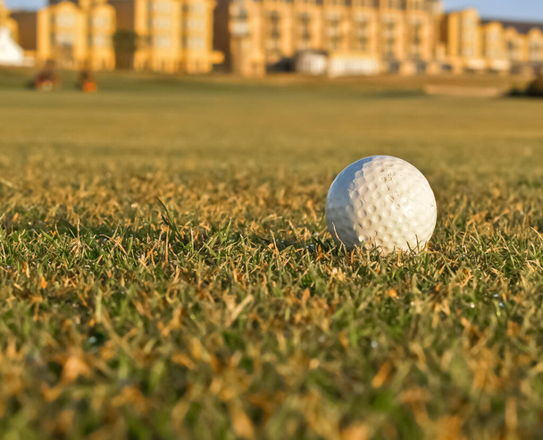 Один білий м'яч для гольфу на передньому плані на майданчику поля для гольфу з дефокусованою будівлею клубу на задньому плані
 - Фото, зображення