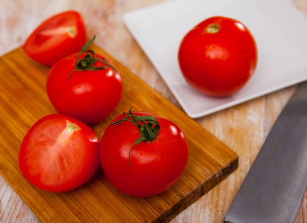 Ripe juicy tomatoes on cutting board on kitchen table. Preparing food concept. - Фото, зображення