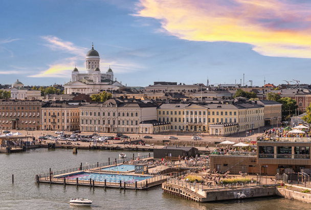 Helsinki, Finlande - 20 juillet 2022 : La cathédrale blanche avec ses dômes verts domine le port, la piscine publique, le restaurant Atlas et le paysage urbain sous le coucher du soleil bleu. - Photo, image