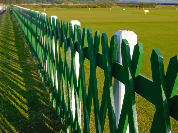 Зеленый и белый деревянный забор вдоль кромки поля для гольфа в Шотландии. - Фото, изображение