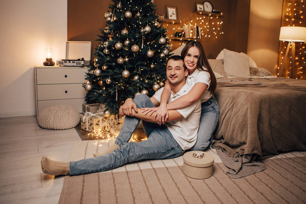 Schöne junge romantische Paar sitzen offene Geschenke präsentiert Girlanden zu Hause gemütliche Inneneinrichtung Neujahr Christbaumschmuck Feiertag Party feiern Winterabend  - Foto, Bild