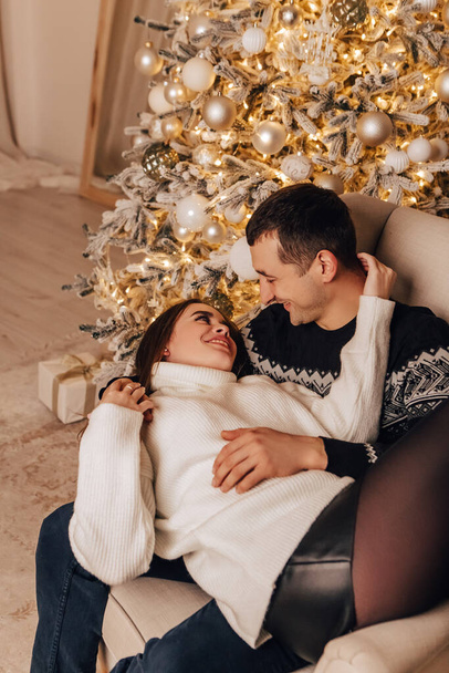 Vertical image lovely young romantic couple sitting lying under blanket, garlands home cosy interior atmosphere New Year Christmas tree decorations holiday party celebrating winter evening  - Foto, Imagem