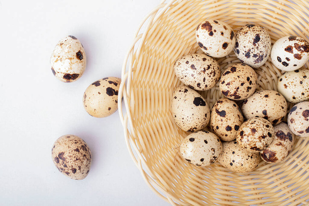 Quail eggs in a wicker plate on a light background. - Foto, afbeelding