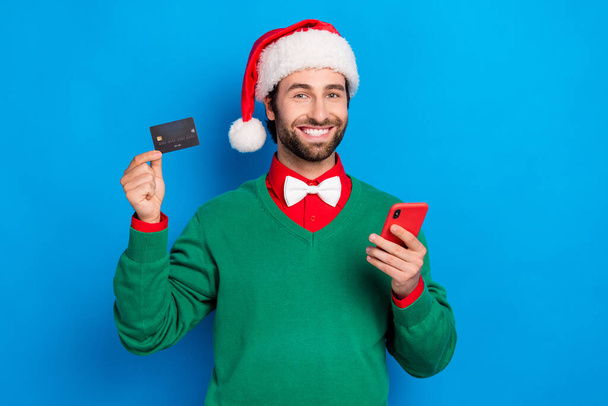 Portrait of cheerful handsome guy hold plastic debit card telephone isolated on blue color background. - Zdjęcie, obraz