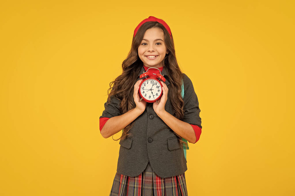 kid in uniform on yellow background. september 1. happy childhood. child with alarm clock. smiling teen girl carry backpack. back to school. knowledge day. education time. - Foto, Bild