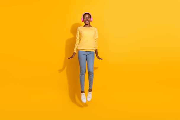 Full length body size view of beautiful trendy cheerful girl jumping listening hit isolated over bright yellow color background. - Фото, изображение